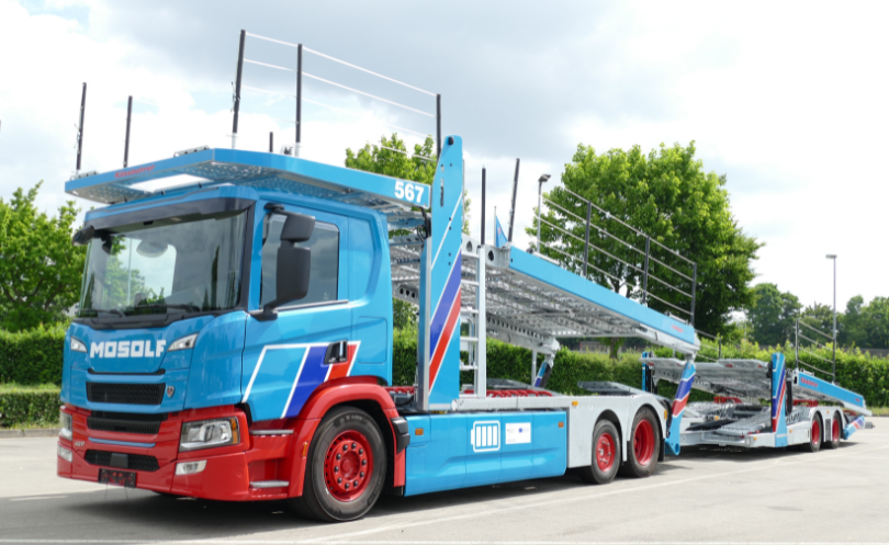 Environment_NHB Ein blau-roter E-LKW steht auf einem Parkplatz.
